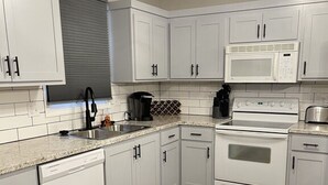 Una cocina moderna con armarios blancos, un lavamanos de acero inoxidable, un microondas, un horno y un lavavajillas.