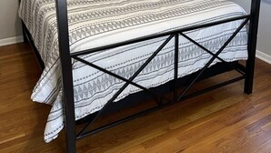 Una cama con dosel de cuatro postes, con un edredón de estampado geométrico, estructura de metal oscuro y suelo de madera.