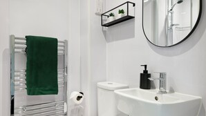 Een moderne badkamer met toilet, wastafel, handdoekrek en een klein plankje met planten.