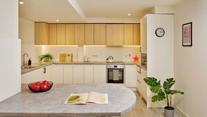 Een moderne keuken met houten kastjes, een inbouwoven en een eethoek met een tafel en stoelen.