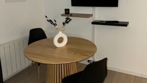 Ein moderner Essbereich mit einem runden Holztisch, schwarzen Stühlen, einer weißen Vase und einem an der Wand befestigten Flachbildfernseher.
