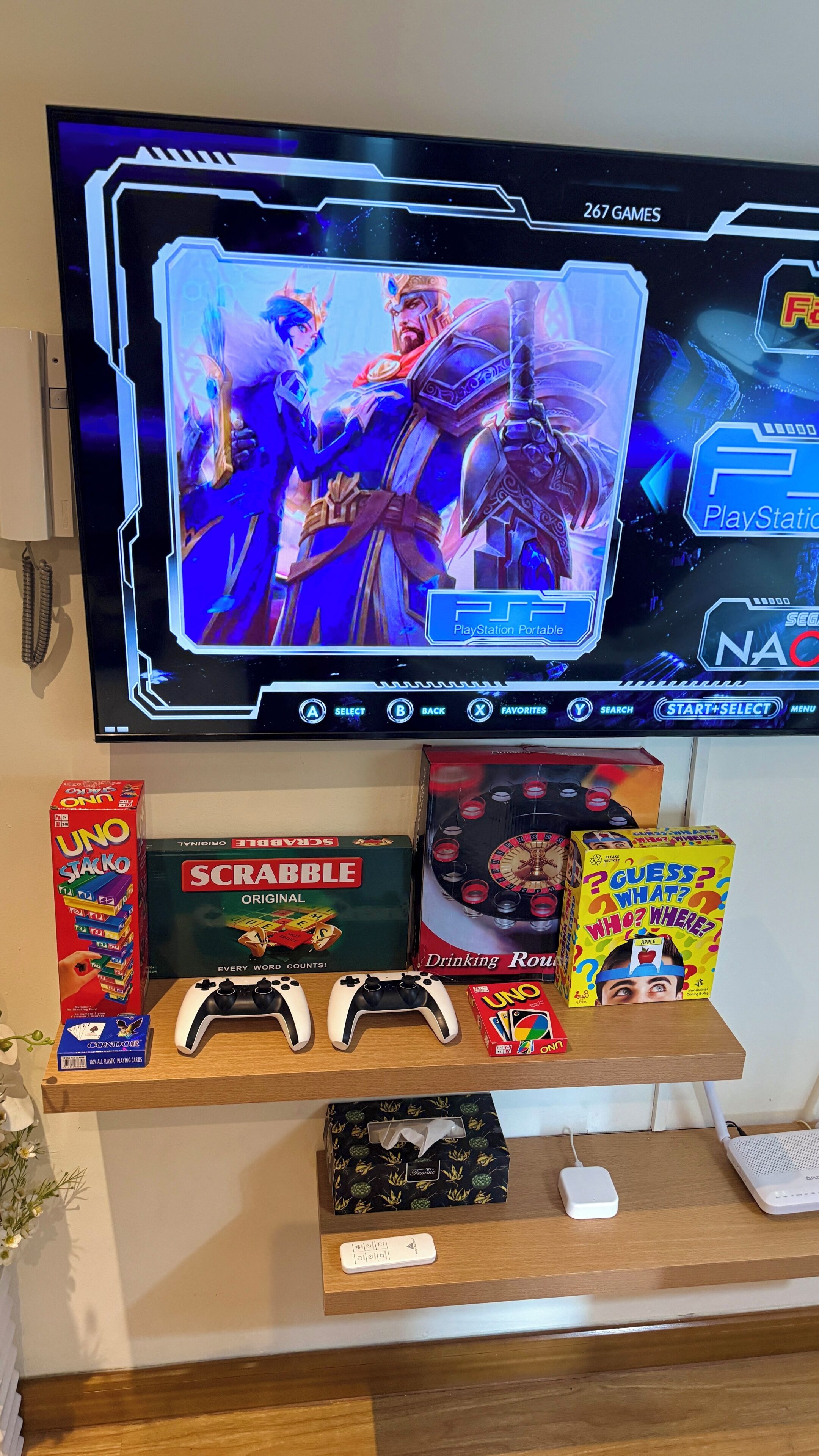 A PlayStation Portable screen displaying a game, with board games UNO, SCRABBLE, and a Guess Who? box on a shelf below.