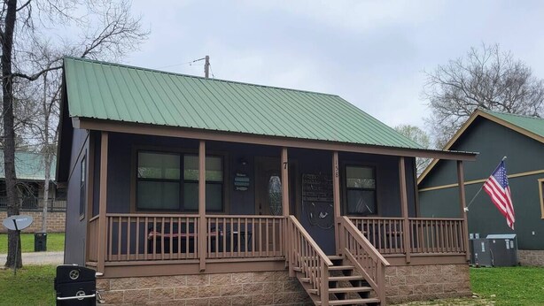A small building with a green roof, a porch with wooden railings, and a flag. - Peaceful lakeside cedar cabin in charming Hot Springs (Hot Springs)