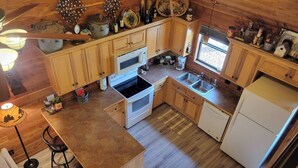 A compact kitchen with wooden cabinets, a central island, a stove, and a refrigerator. - Peaceful lakeside cedar cabin in charming Hot Springs (Hot Springs)