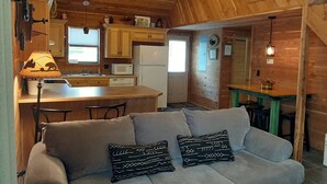 A cozy cabin interior with a sofa, a dining table, and a kitchen area. - Peaceful lakeside cedar cabin in charming Hot Springs (Hot Springs)