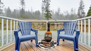 A deck with two blue chairs, a wood-burning stove, and a view of a forested area. - Limpy Creek Access! Family Retreat in Grants Pass (Grants Pass)