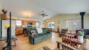 A spacious living room with a green sofa, wooden furniture, a TV, and a kitchen in the background.
