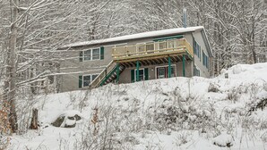 A two-story house with a balcony, surrounded by snow-covered trees.