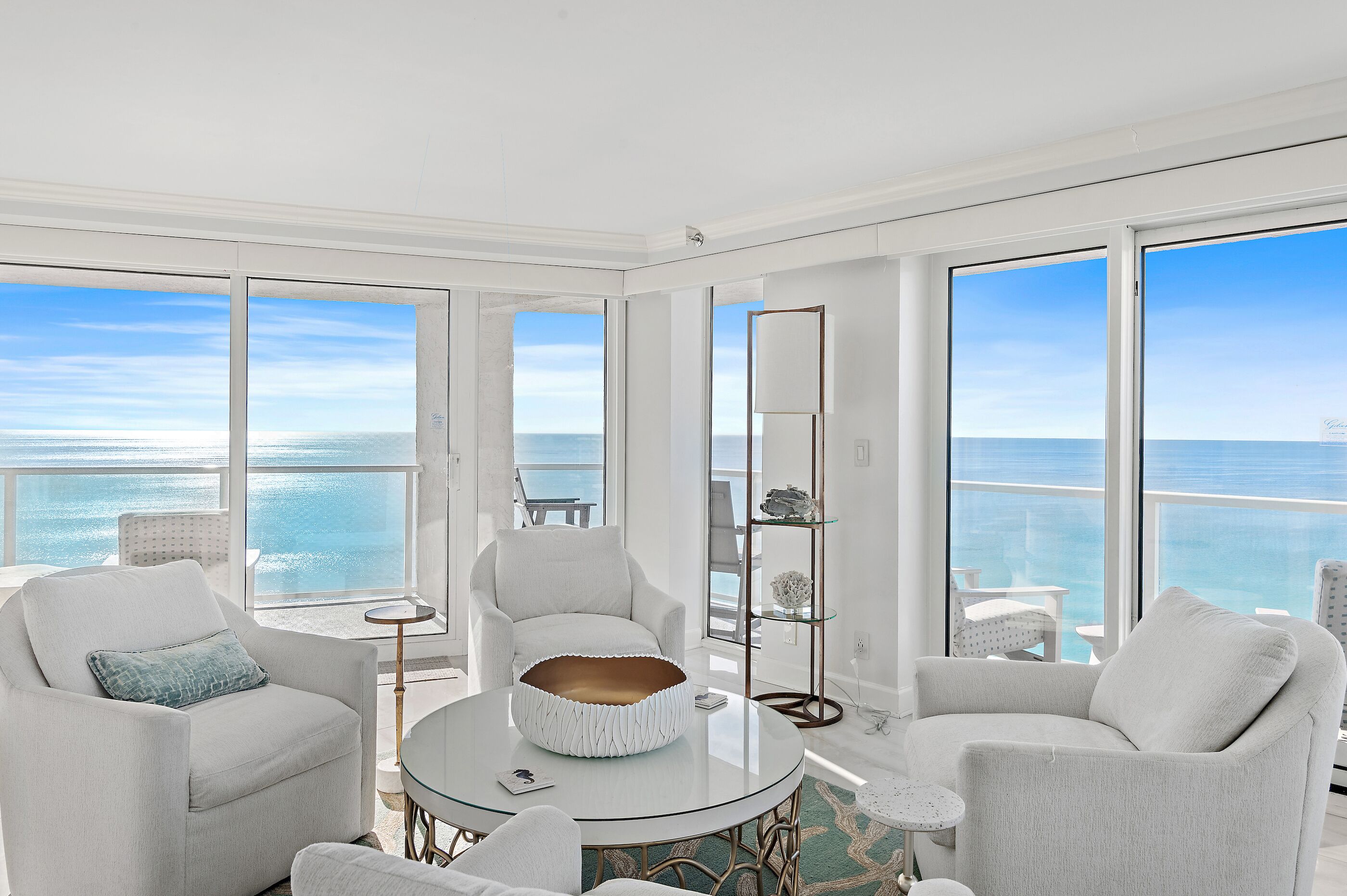 A spacious balcony with a clear view of the ocean, furnished with white chairs and a round table.