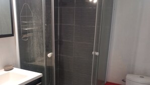 Ein Badezimmer mit einer gläsernen Duschkabine, einer weißen Toilette und einem Waschbecken mit dunkler Arbeitsplatte.