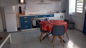 Eine kleine Küche mit Essbereich, weiß gefliester Boden und ein Fenster mit Vorhängen.