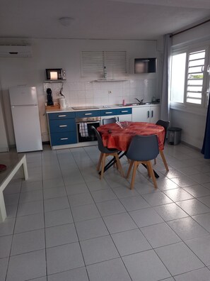 A compact kitchen with a dining area, white tiled floor, and a window with curtains. - Functional duplex with superb sea view (Les Trois-Îlets)