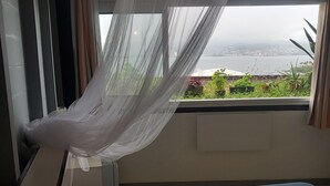 Ein Zimmer mit einem Bett, einem Fenster mit Meerblick und einem Deckenventilator.