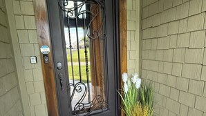 Een donkerhouten deur met een decoratief metalen hekwerk, een deurmat en een bloempot.