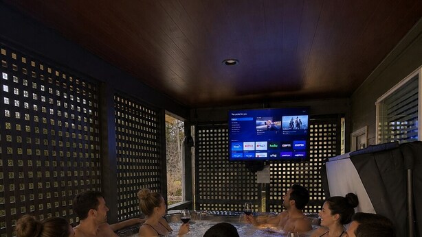 Een bubbelbadgedeelte met mensen die ontspannen, een televisiescherm en een fles wijn op een bijzettafeltje.