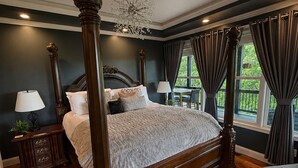 Een hemelbed met een kroonluchter, donkere wanden en uitzicht op groen.