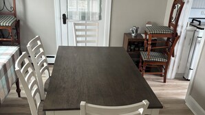 A dining area with a dark wooden table and white chairs, a chandelier, and a kitchen in the background. - Quaint 2-bedroom house wanting your TLC in charming Hammondsport (Hammondsport)