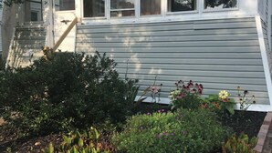 A two-story house with a front porch, a small garden with various plants and flowers, and a visible staircase leading to the entrance. - Quaint 2-bedroom house wanting your TLC in charming Hammondsport (Hammondsport)