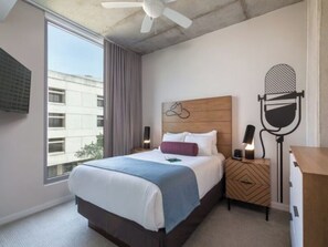 A hotel room with a large bed, a nightstand, a desk, a ceiling fan, and a view of a building outside. - SXSW Ready! Luxe 2BR Condo in the Heart of Austin (Austin)