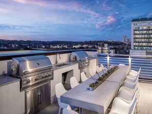 An outdoor kitchen with a grill and a dining area with chairs, overlooking a cityscape at dusk. - SXSW Ready! Luxe 2BR Condo in the Heart of Austin (Austin)