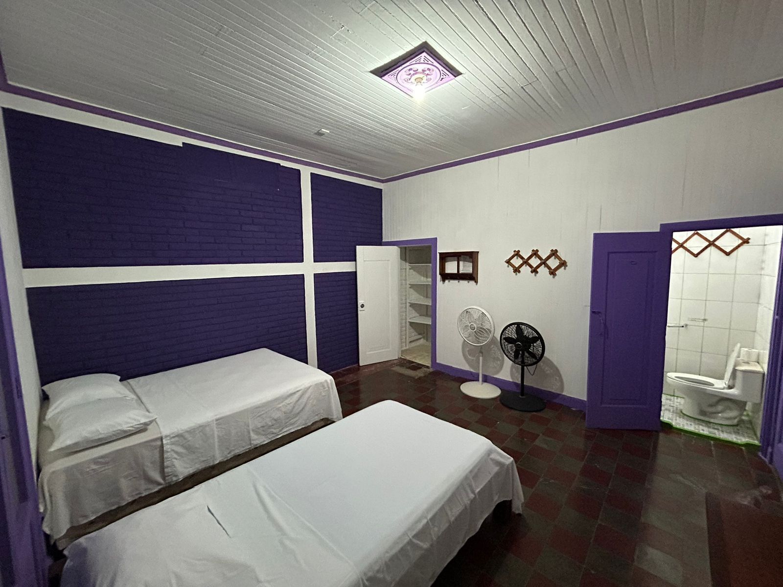 Una habitación con dos camas, un ventilador, un inodoro y una ventana pequeña.