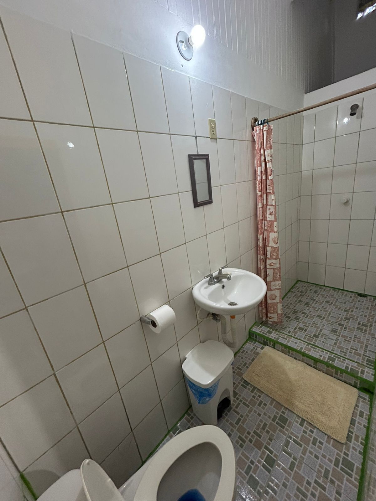 Casa de banho com paredes azulejadas em branco, uma pia branca, sanita e zona de duche.