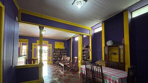 Une pièce avec un sol à carreaux, des chaises en bois, une table recouverte d’une nappe et une bibliothèque.