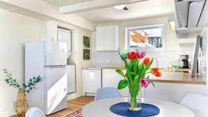 Une cuisine moderne avec des meubles blancs, un réfrigérateur blanc et un coin repas comprenant une table ronde et des chaises.