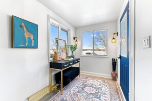 A hallway with a blue door, a black console table with drawers, a patterned rug, and artwork on the walls. - Private Basement Suite | Minutes to Downtown (Charlottetown)
