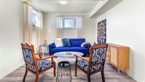 Un salon avec un canapé bleu, deux fauteuils à motifs, une petite table ronde et un meuble en bois.