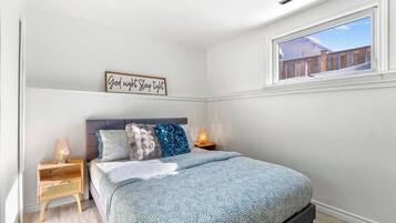 Ein Schlafzimmer mit einem Bett, zwei Nachttischen, einem Fenster und einem Wandzeichen.