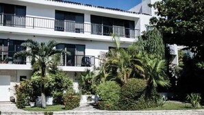 A two-story building with balconies, surrounded by lush greenery and palm trees.