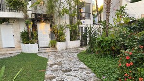 A stone pathway leading to a building entrance, surrounded by lush greenery and flowering plants.