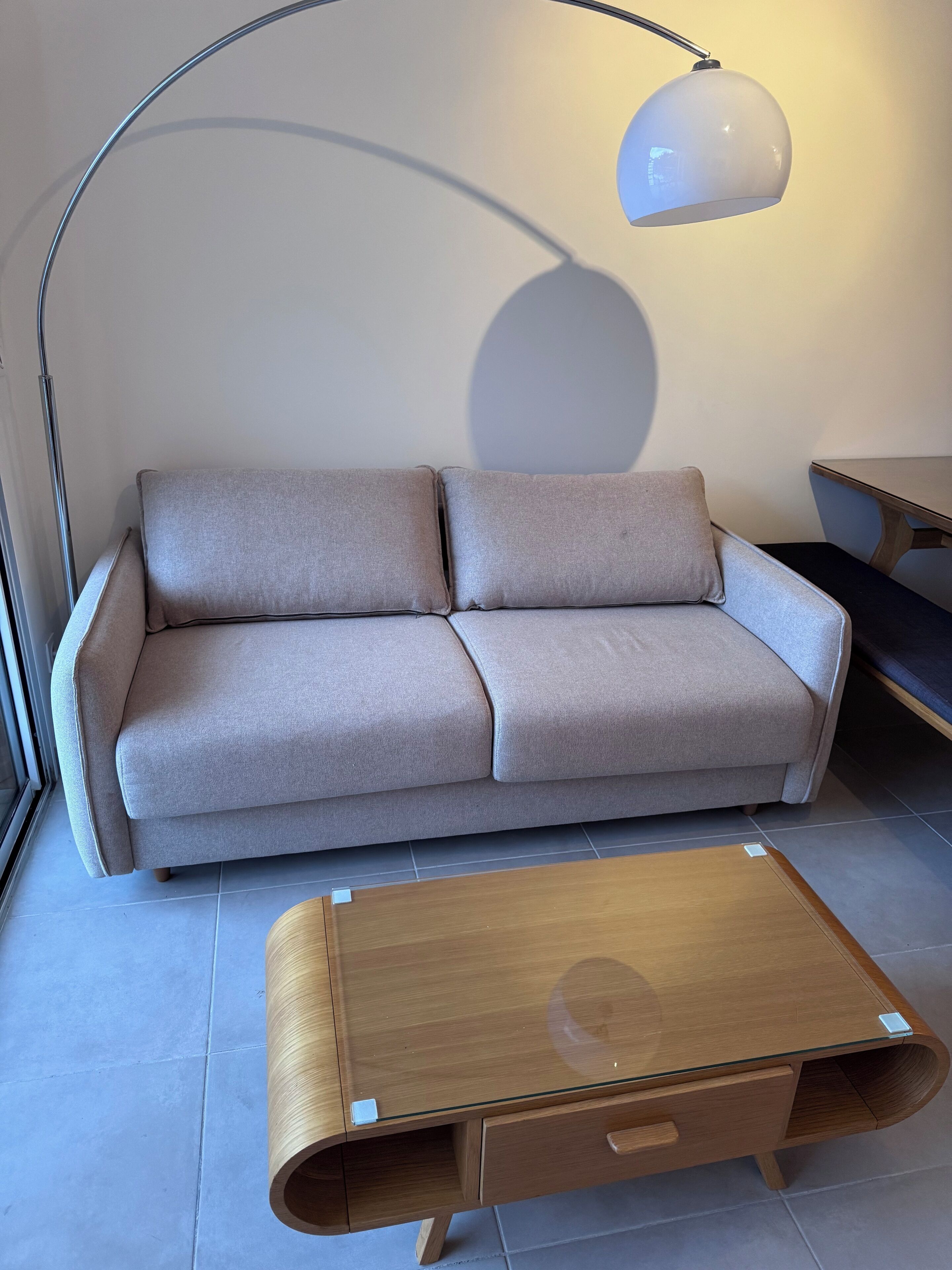 Ein modernes Wohnzimmer mit einer grauen Couch, einem Holztisch und einer Stehlampe.