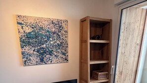 A room with a flat-screen TV on a wooden stand, a wooden cabinet with shelves, and a large abstract painting on the wall. - New apartment near Prorel (Briançon)