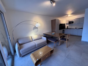 Ein modernes Wohnzimmer mit Sofa, Couchtisch und Esstisch. Es gibt eine Küchenzeile mit Schränken und einer Mikrowelle.