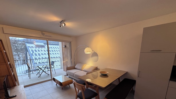 A modern kitchen with a dining area, a sofa, and a balcony with a view of snow-covered trees. - New apartment near Prorel (Briançon)