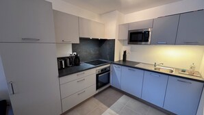 A modern kitchen with white cabinets, a microwave, a sink, and a coffee maker. - New apartment near Prorel (Briançon)
