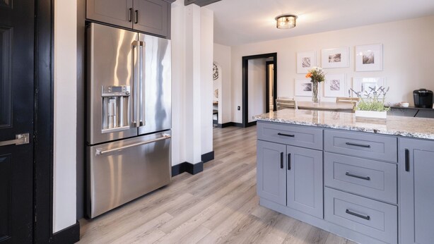 Una cocina moderna con armarios grises, un refrigerador de acero inoxidable y piso de madera.