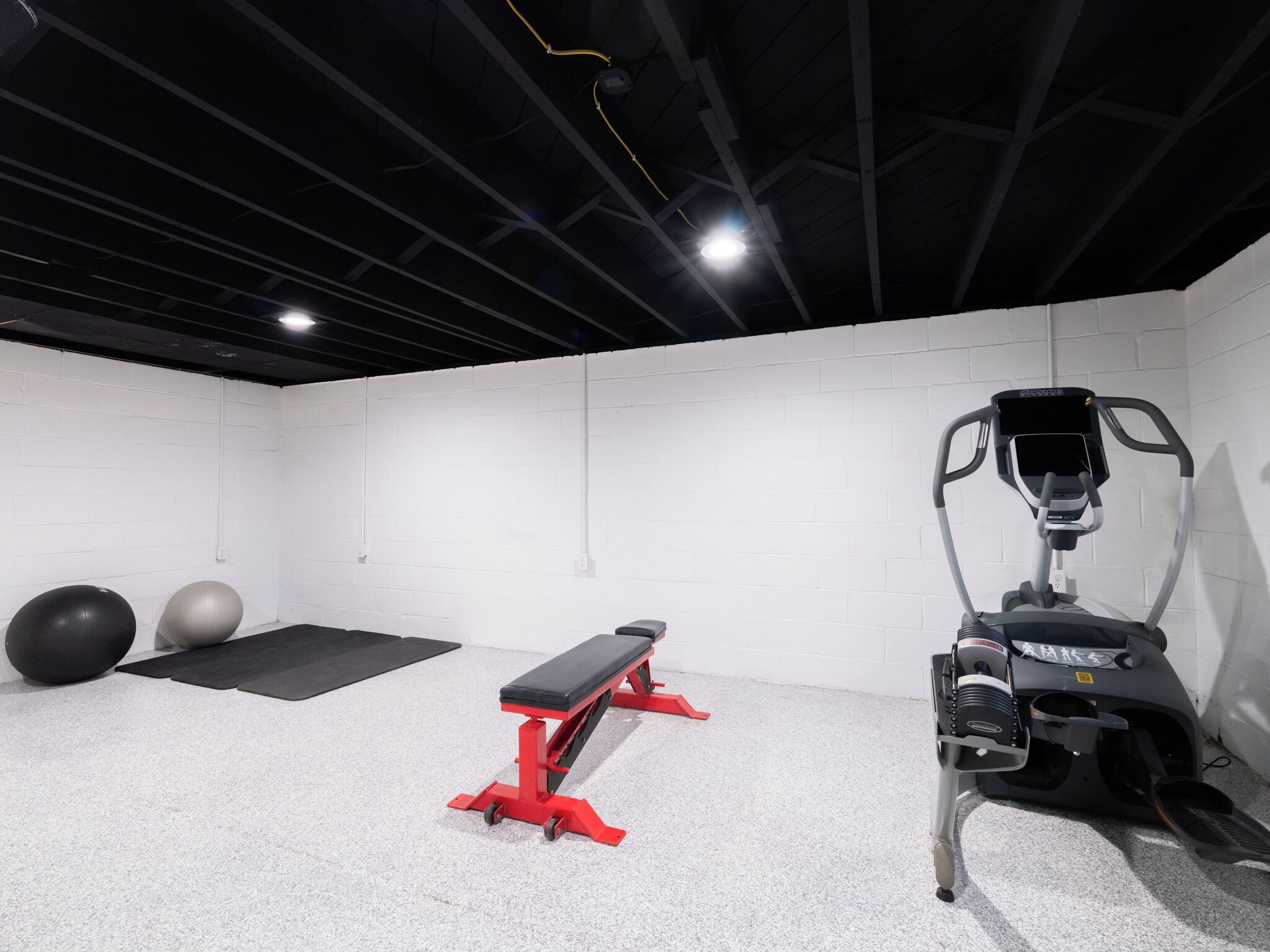 Une salle de sport avec un banc rouge, des ballons d’exercice et un vélo d’appartement.