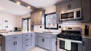 Una cocina moderna con gabinetes grises, electrodomésticos de acero inoxidable y un ventanal que proporciona luz natural.