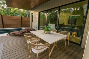 An outdoor patio with a wooden deck, a white table with wicker chairs, a small pool, and a glass-enclosed kitchen area. - Grand 11BR Compound! Near Downtown Vibes! (Austin)