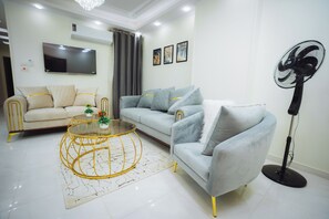 A modern living room with a sofa, a coffee table, a TV, and a standing fan. - Star Luka offers a sophisticated accommodation experience (Luxor)