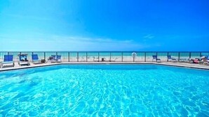 Una piscina azul cristalina con sillas de descanso y una valla.