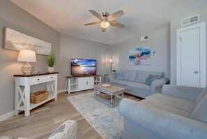 Ein Wohnzimmer mit Deckenventilator, Fernseher, Sofa, Couchtisch und einer Konsole mit Lampe.