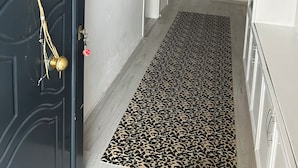Un couloir avec une porte noire, un tapis à motifs léopard et un meuble blanc.
