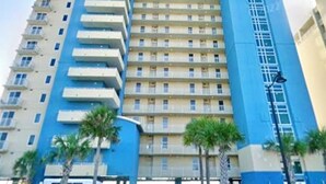 Un hotel de varios pisos con fachada azul y color crema, una entrada central y palmeras al frente.