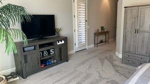 Una habitación con una televisión sobre un mueble de madera, una puerta con persianas, una mesita con una planta y un armario.