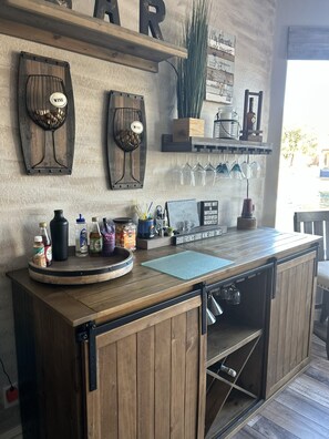 Un coin bar rustique avec des étagères en bois où sont exposés des verres à vin, une enseigne sur le vin et une autre indiquant : « Mes régions viticoles préférées ».