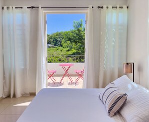 A bedroom with a bed, a view of a balcony with a table and chairs, and curtains on the windows. - Spacious Family Home Near Beaches, Surf, Restaurants & Nature (rincón)